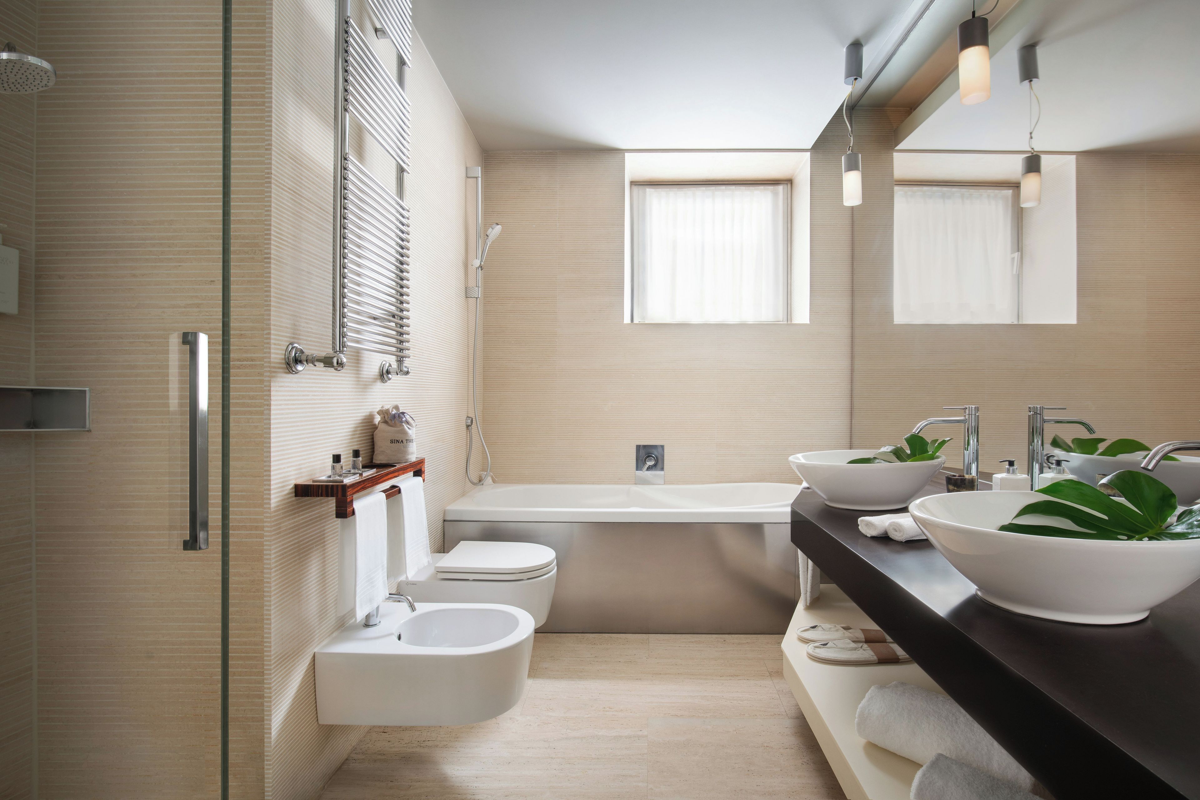 Een moderne badkamer met een badkuip, twee wastafels, een toilet met douchefunctie en een douche.