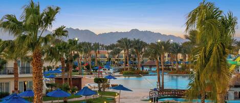 Un área de piscina en un resort con palmeras, sillas de descanso y sombrillas.