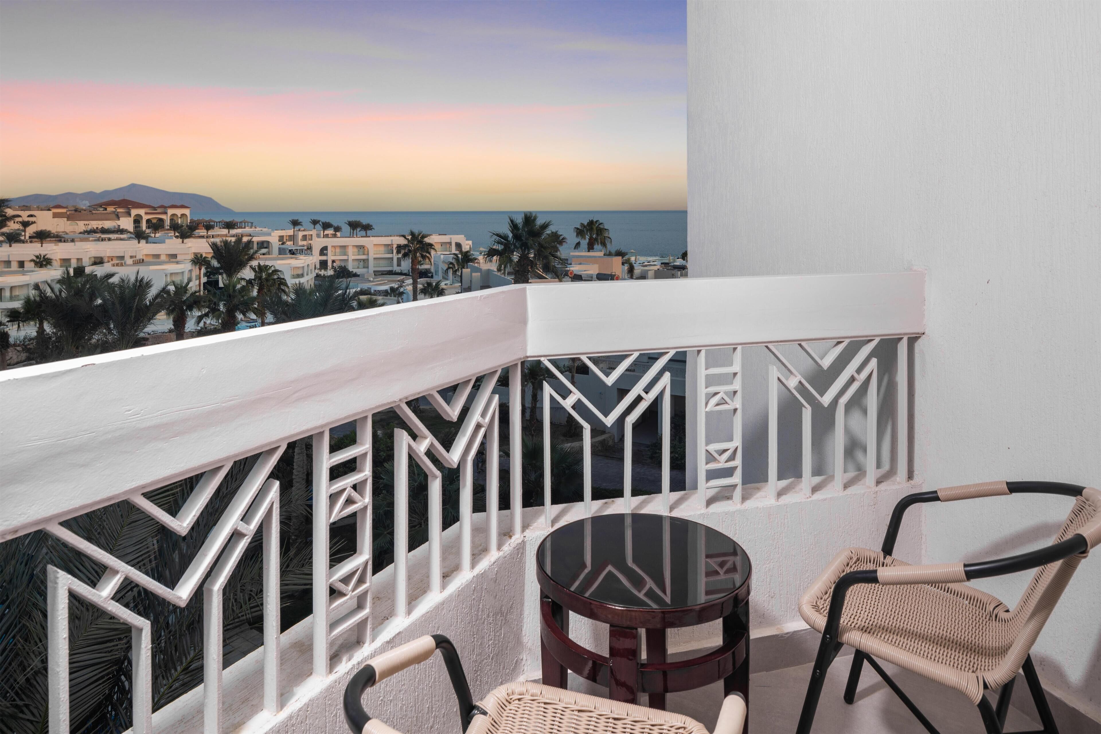 A balcony with a geometric railing, two wicker chairs, and a small round table.