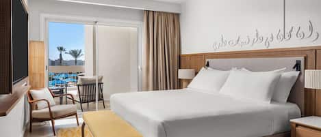 Habitación de hotel con cama, escritorio, silla, ventana que ofrece vistas a palmeras y un ventilador de techo.