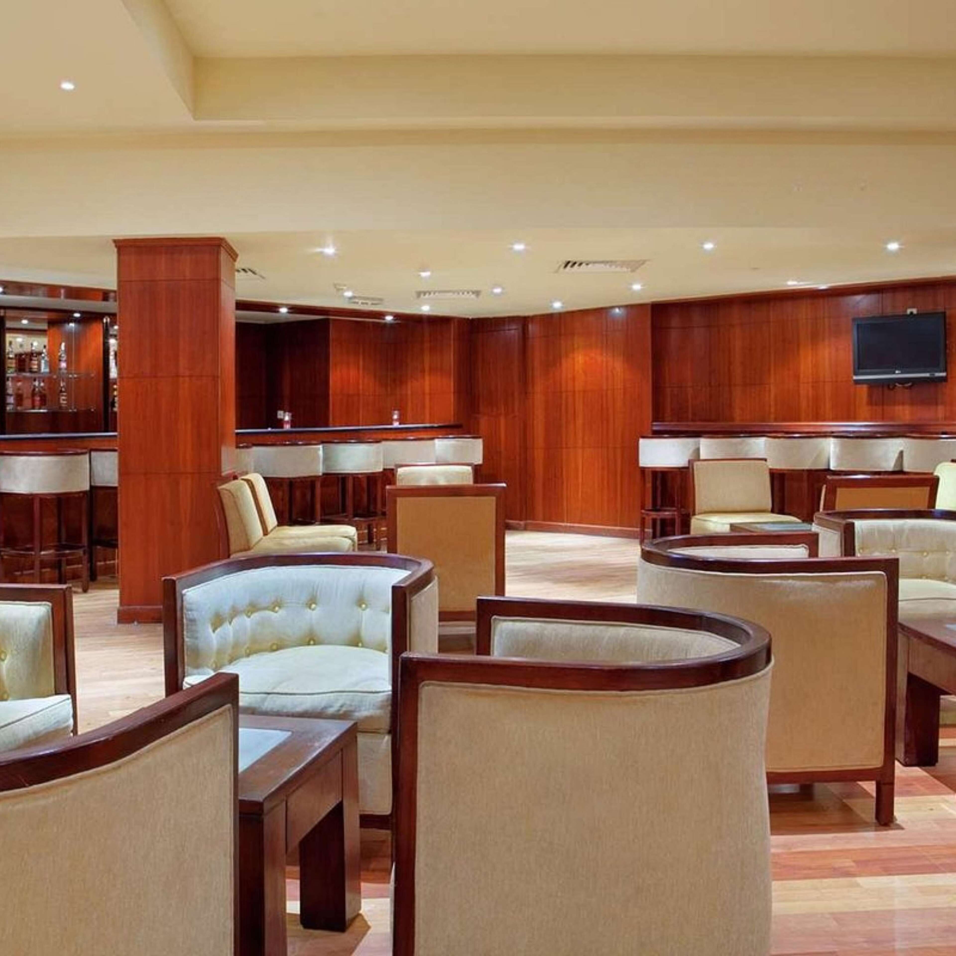 A spacious lobby with multiple seating areas, a bar, and a flat-screen TV mounted on the wall.