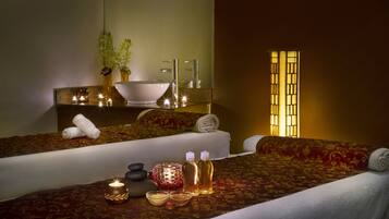 A well-lit spa room with a large mirror, a sink, and a bed with a red patterned bedspread.