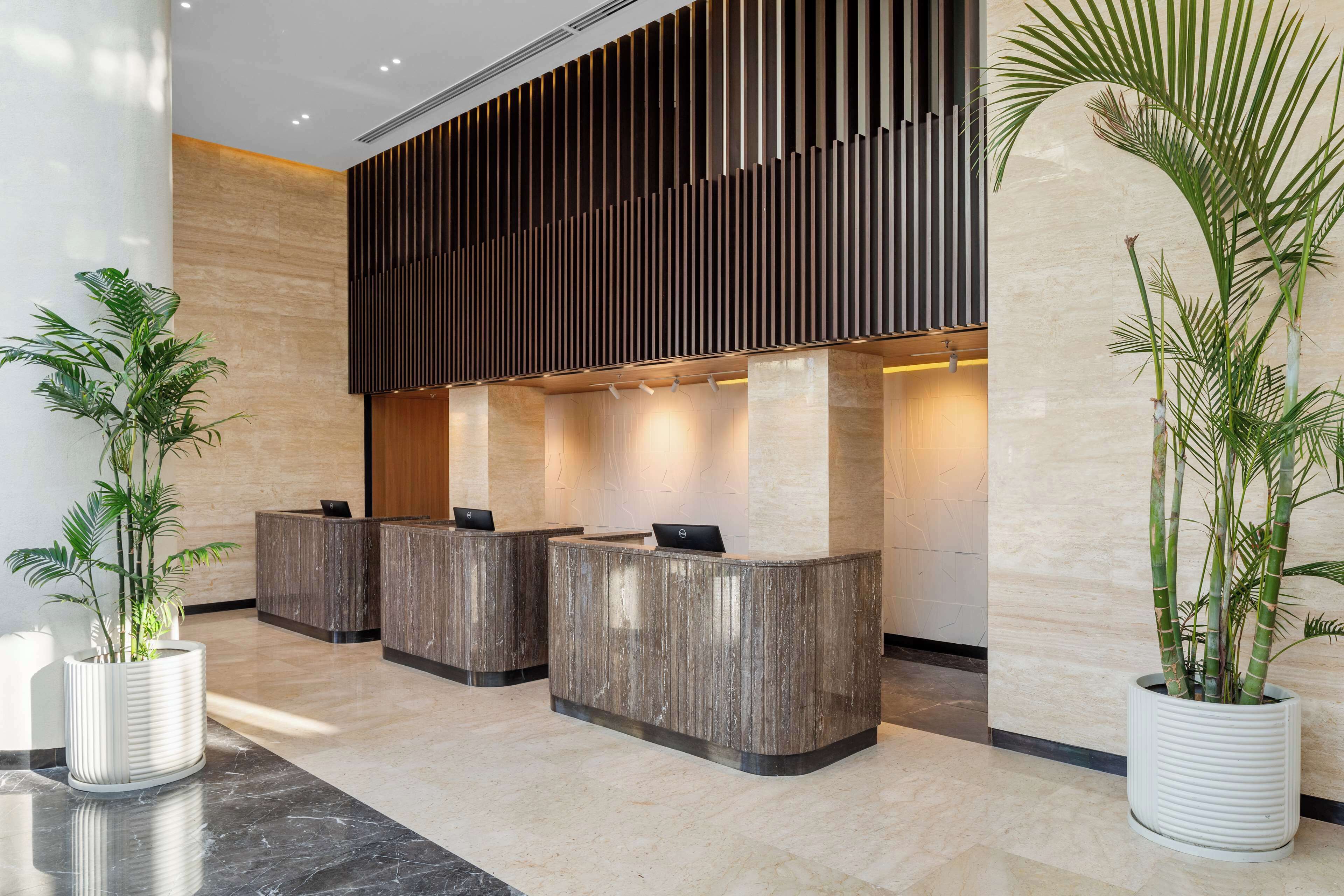 A reception area with three wooden reception desks, a vertical slatted wall, and two large potted plants.