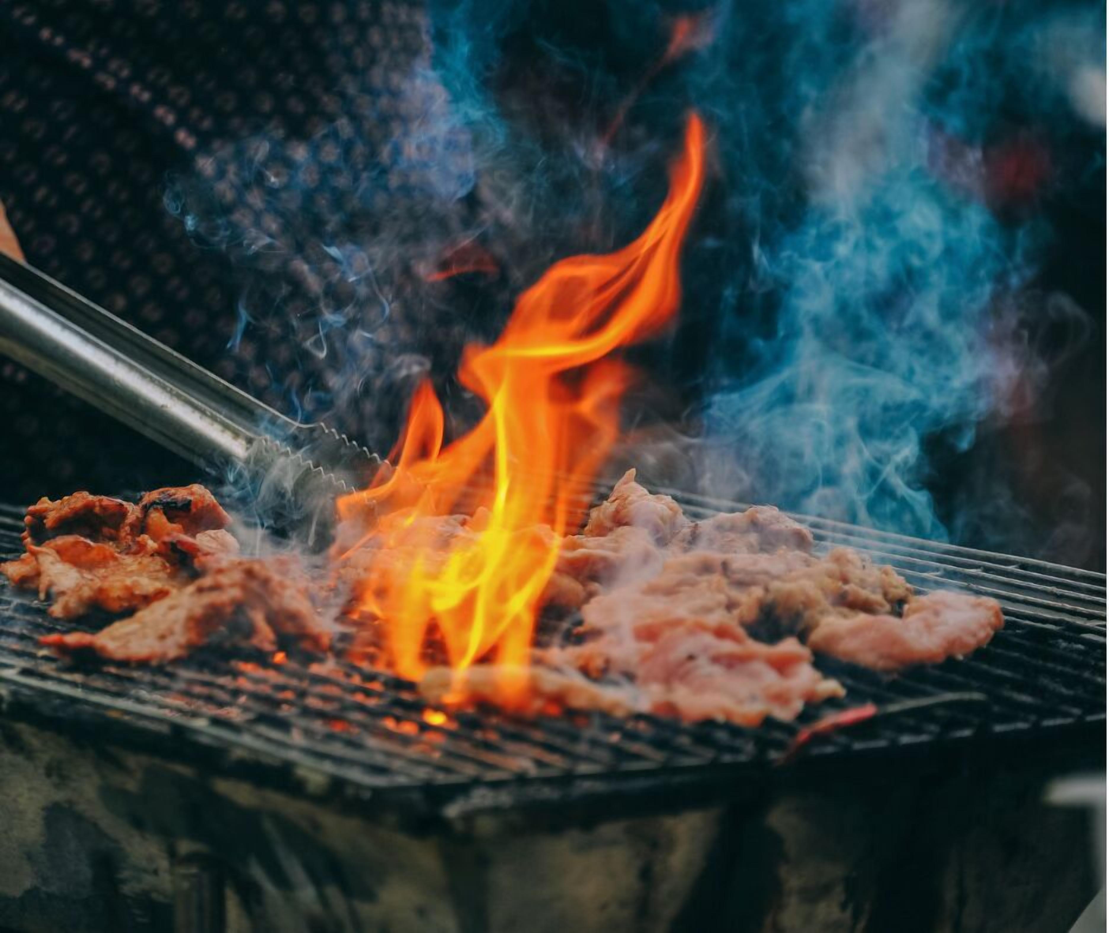 Una parrilla con carne asándose sobre fuego vivo.