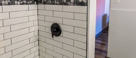 A modern bathroom with white tiled walls, a black showerhead, a built-in toilet, and a white towel on the floor.