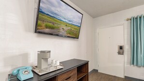 A room with a mounted TV displaying a landscape, a coffee maker, a telephone, and a door with a curtain. - Bel Aire Motel (Missoula)