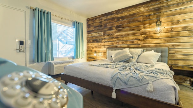 A bedroom with a wooden headboard, a bed with a white quilt, and a bedside table with a lamp. - Bel Aire Motel (Missoula)