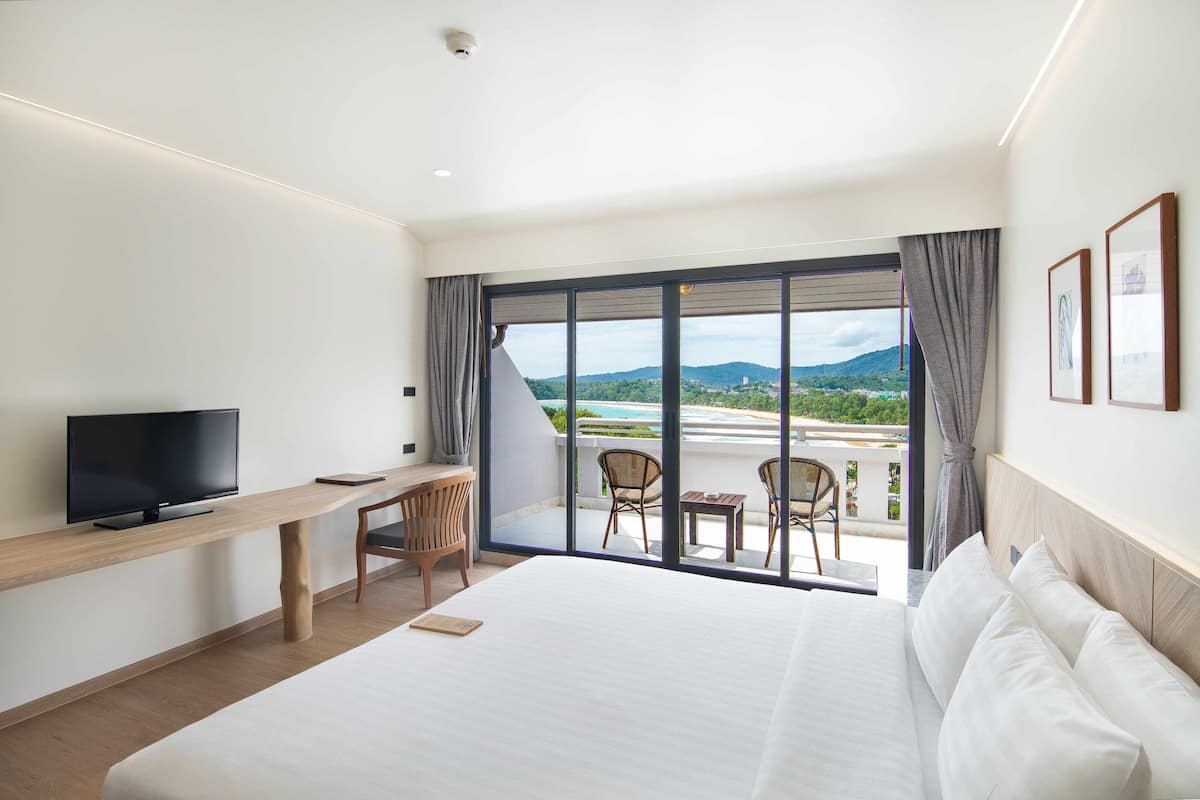 Una habitación de hotel con una cama grande, un escritorio con televisor y un balcón con sillas y una mesa.