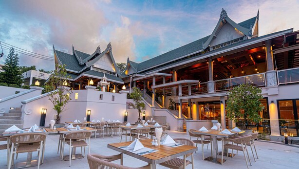 An outdoor dining area with multiple tables and chairs, a staircase leading to an upper level, and a building with traditional architectural features.