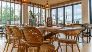 A restaurant with wicker chairs and tables, large windows, and a view of the city.