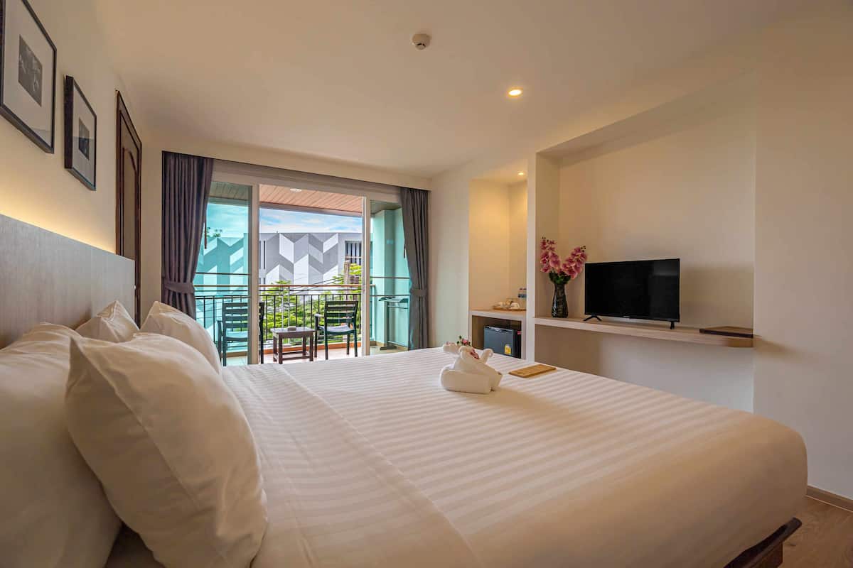 Habitación de hotel con una cama grande, televisión, escritorio pequeño y balcón con vista a la ciudad.