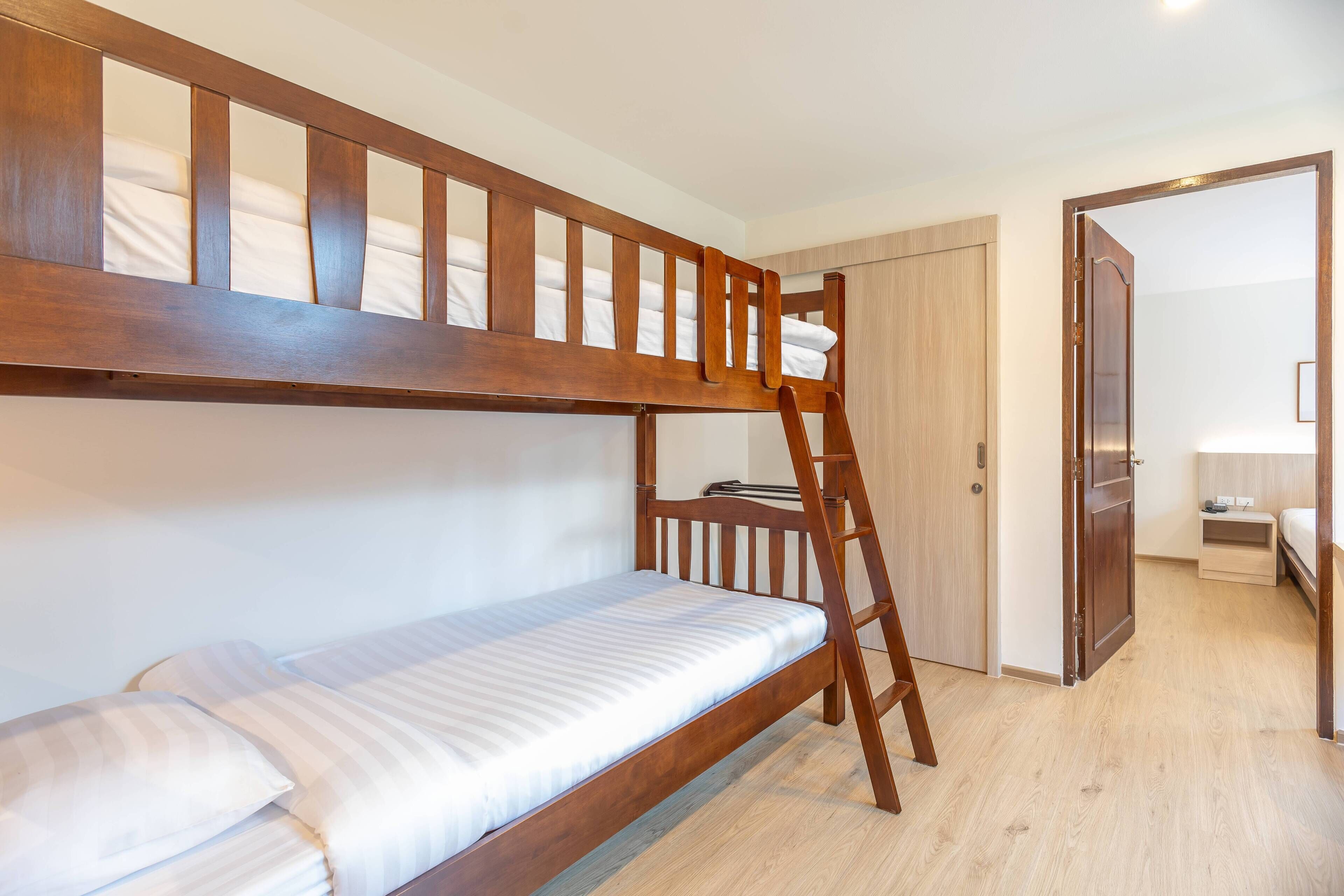 A bunk bed with a ladder, a wooden door, and a small bedside table with a lamp.
