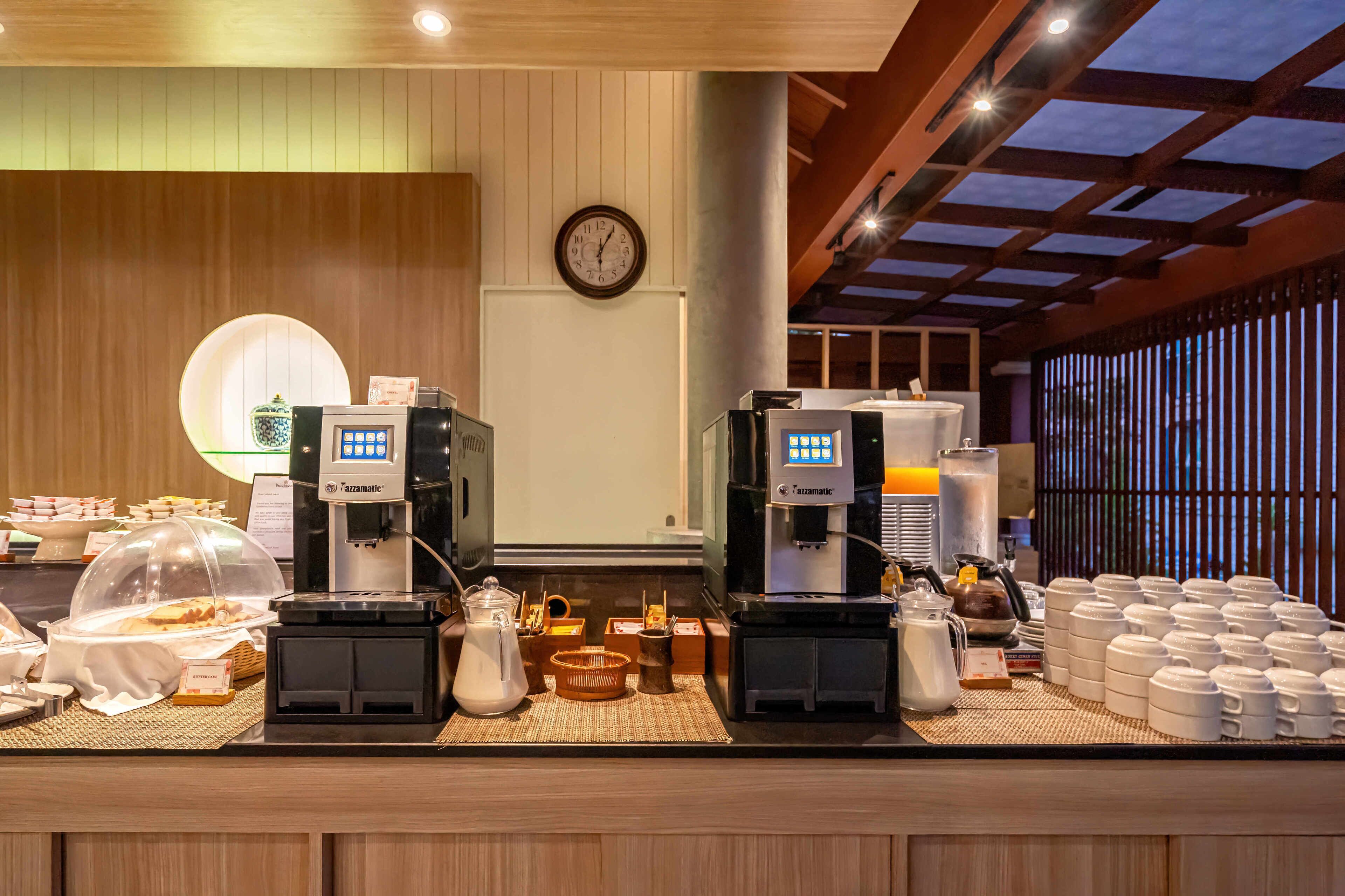 Una barra de desayuno con máquinas de café, un reloj y diferentes opciones para el desayuno.