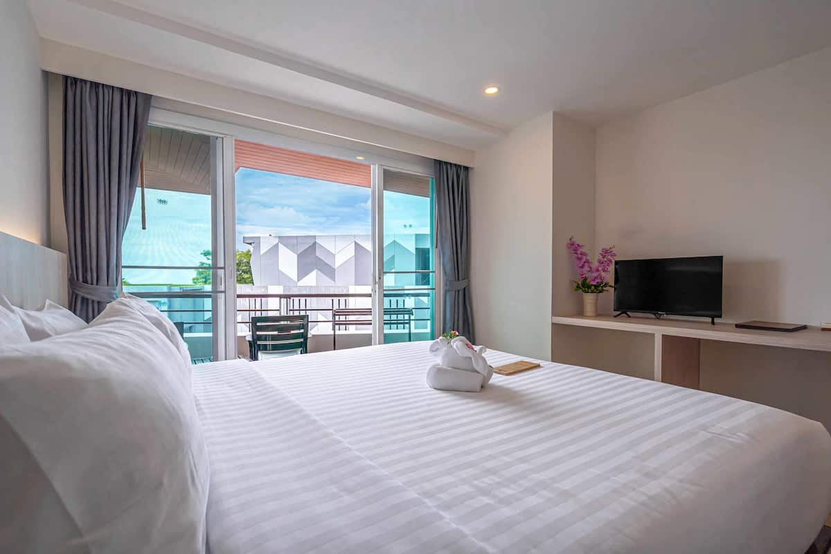 Habitación de hotel con una cama grande, un televisor en un mueble bajo y un balcón con vistas.