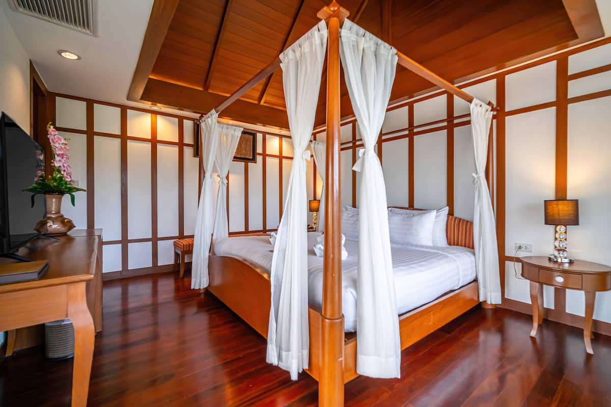 Una cama con dosel y cuatro columnas con ropa blanca, un cabecero de madera y una mesita de noche con lámpara.