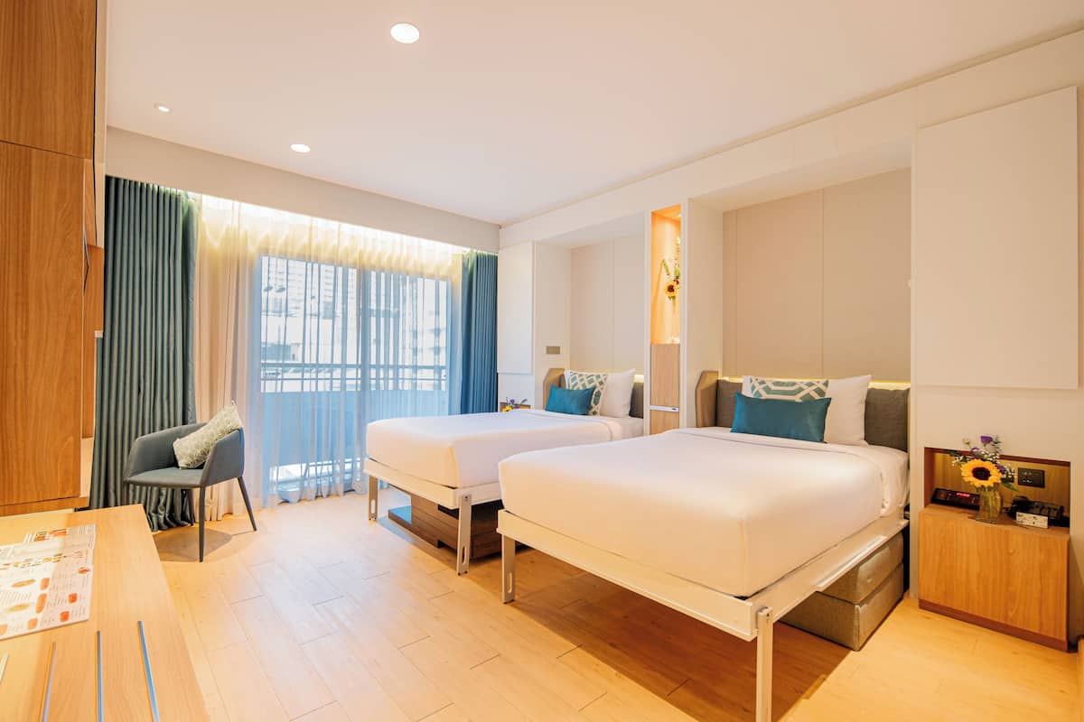 A hotel room with two beds, a desk, a chair, a nightstand, and a window with curtains.