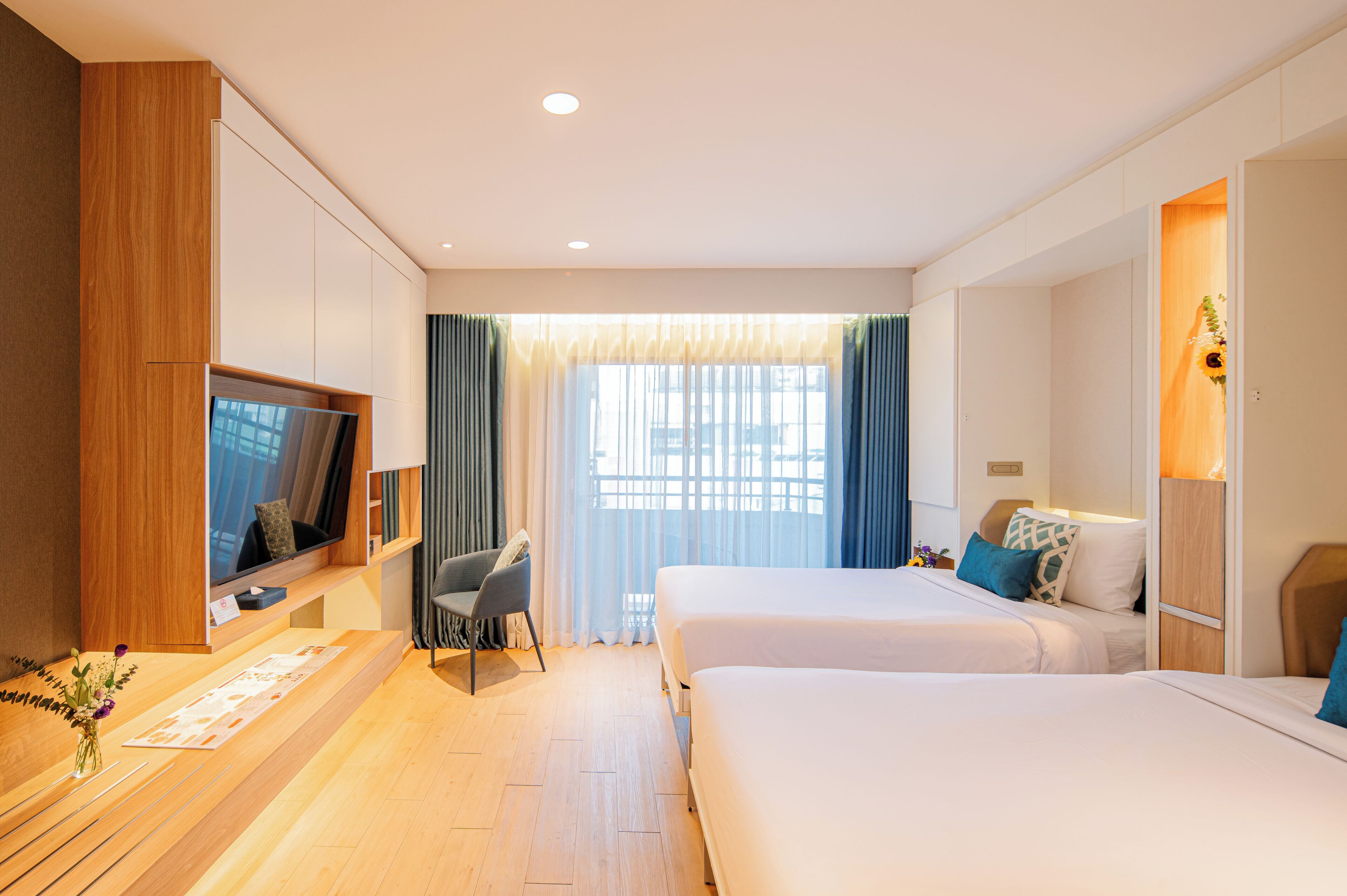 Habitación de hotel con dos camas, televisor, escritorio con silla y un amplio ventanal con cortinas.