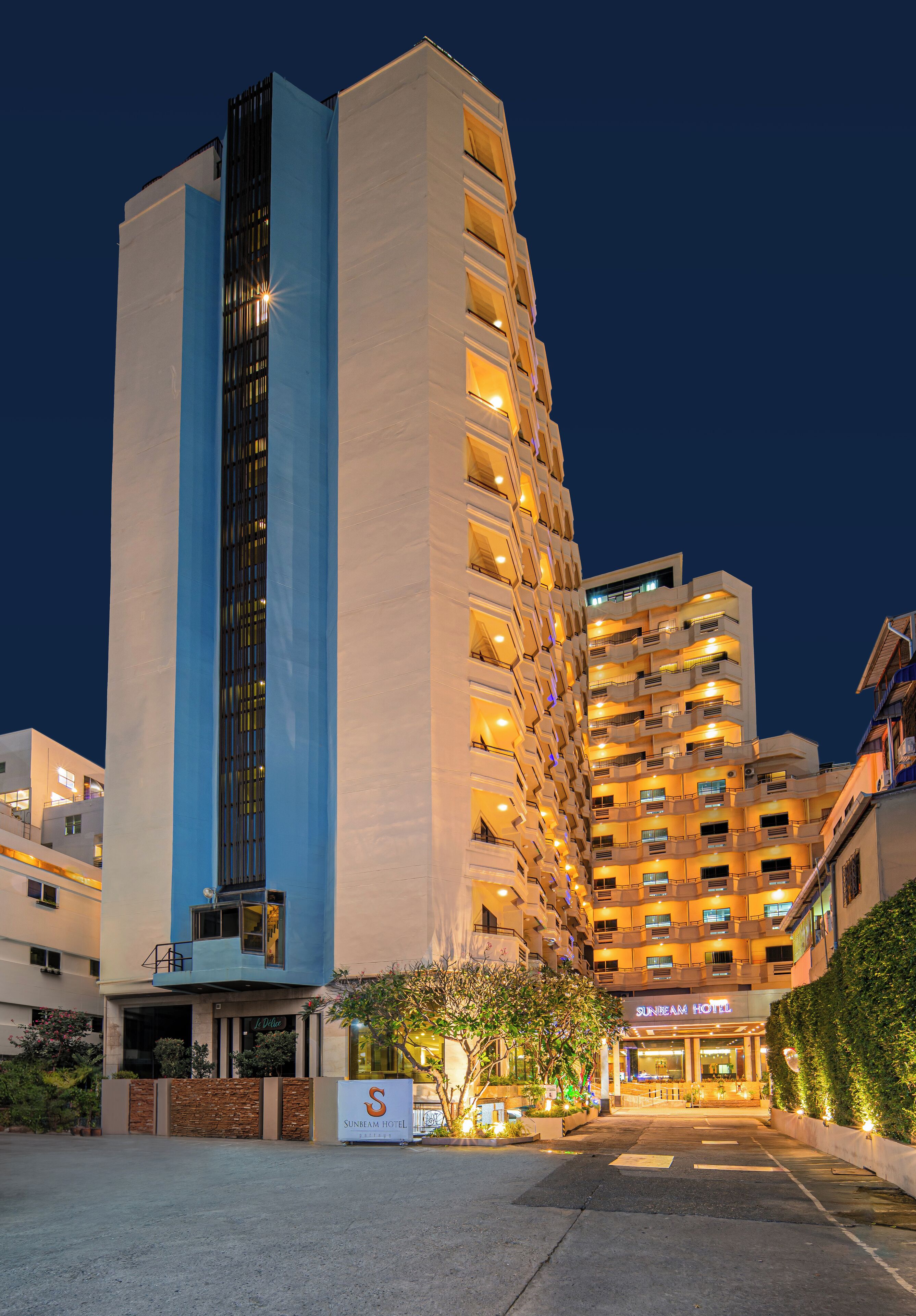 A multi-story hotel with a prominent vertical blue stripe, multiple balconies, and a well-lit entrance.