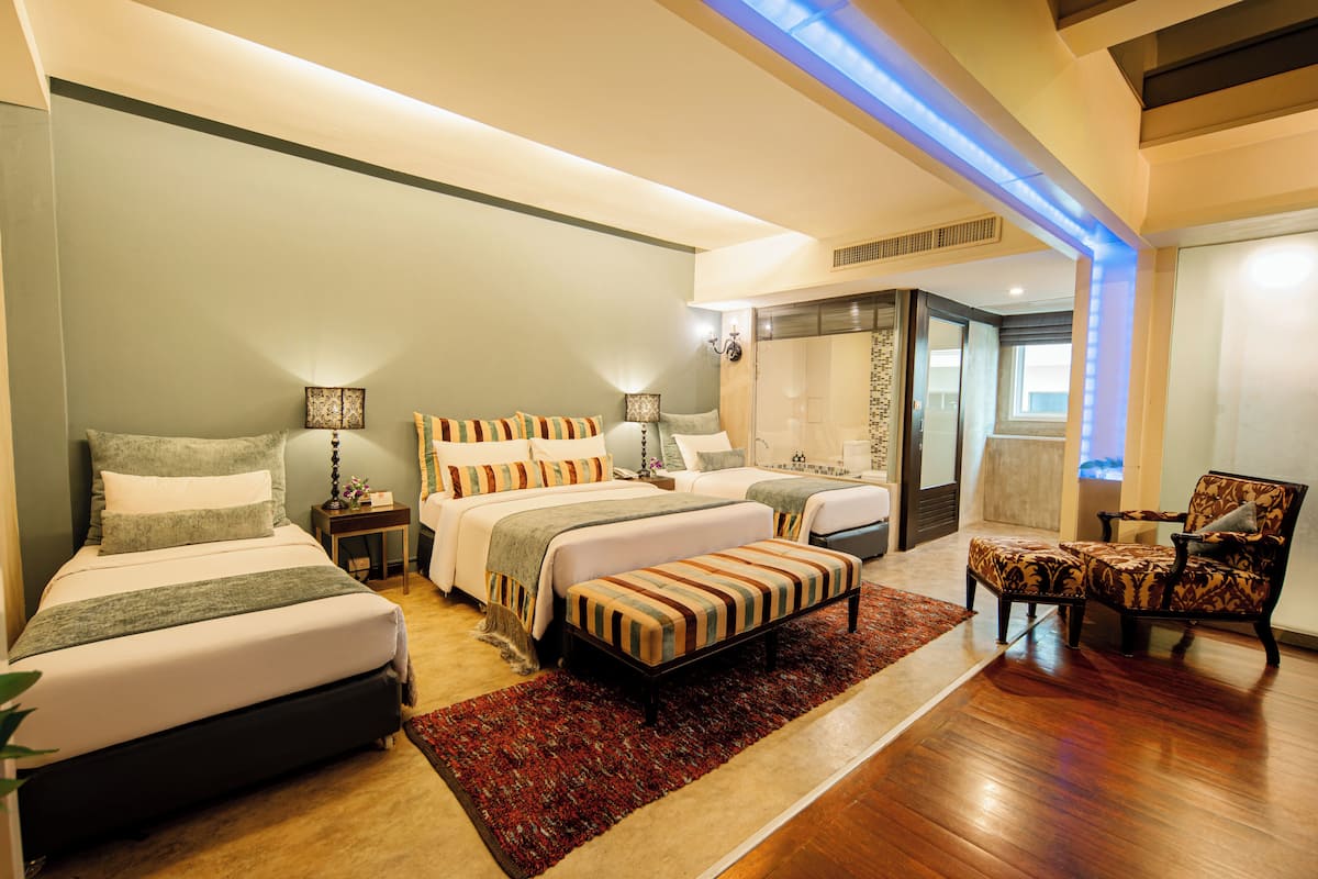 A modern hotel room with two beds, a sitting area, and a shower.