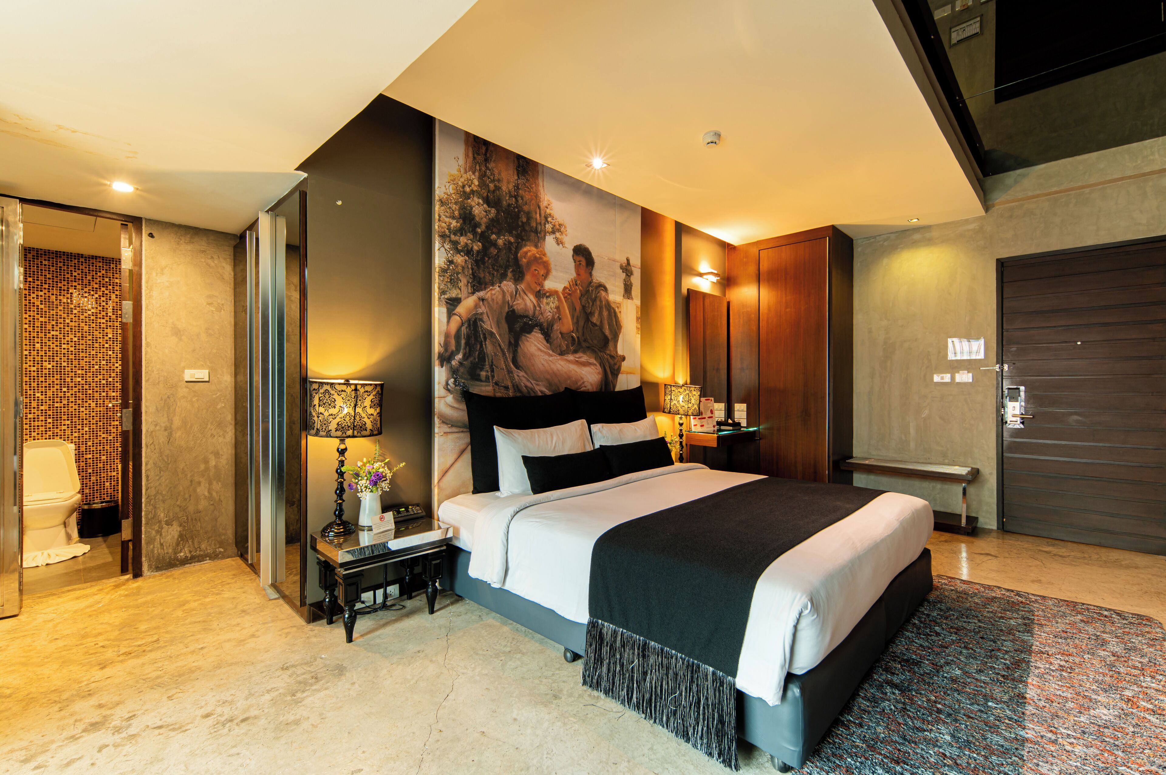 A modern bedroom with a large bed, a nightstand, a wall-mounted lamp, and a door with a handle.