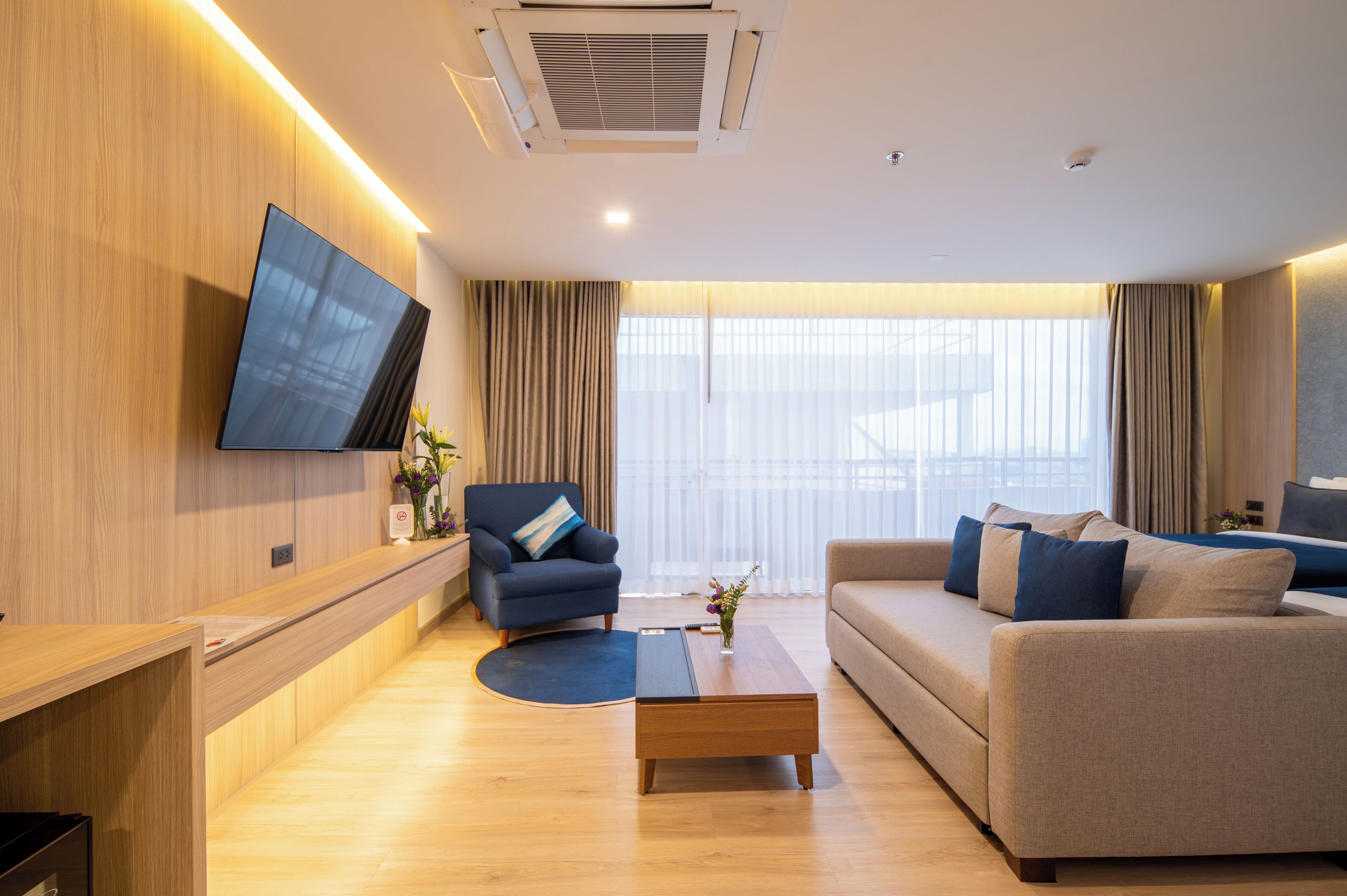 Een moderne woonkamer met een flatscreen televisie aan de muur, een bank, een fauteuil en een salontafel.