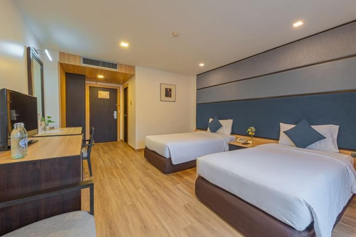 A hotel room with two beds, a desk, a chair, a TV, and a small table with a bottle and a plant.