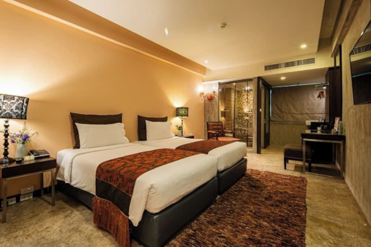 A modern hotel room with a large bed, bedside tables, a desk, and a bathroom visible through an open door.