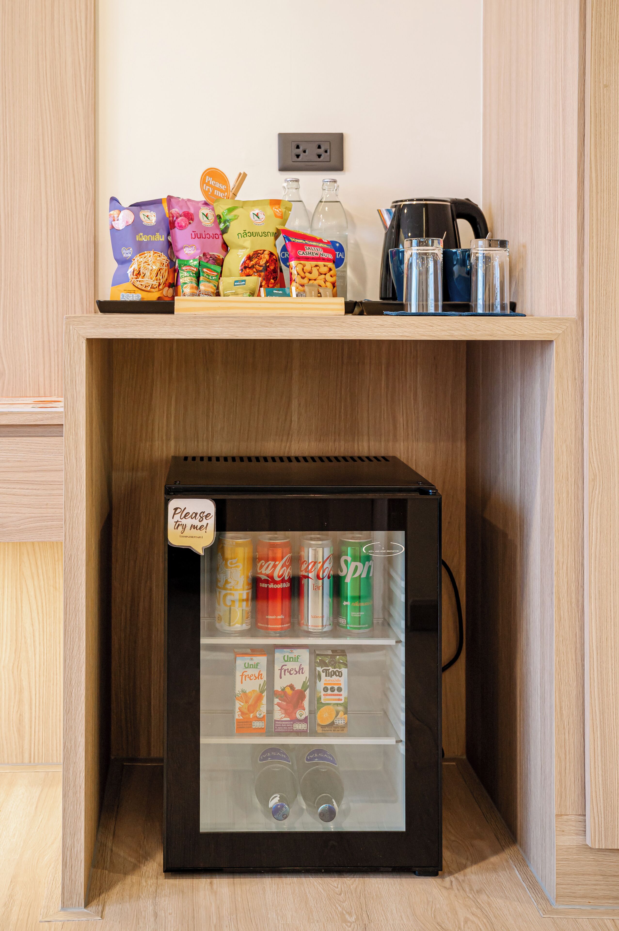 Een kleine koelkast gevuld met drankjes en snacks, een koffiezetapparaat en een waterkoker op een plank erboven.