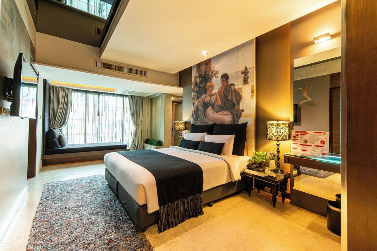 A modern hotel room with a large bed, a seating area with a view, a desk with a lamp, and a large painting on the wall.