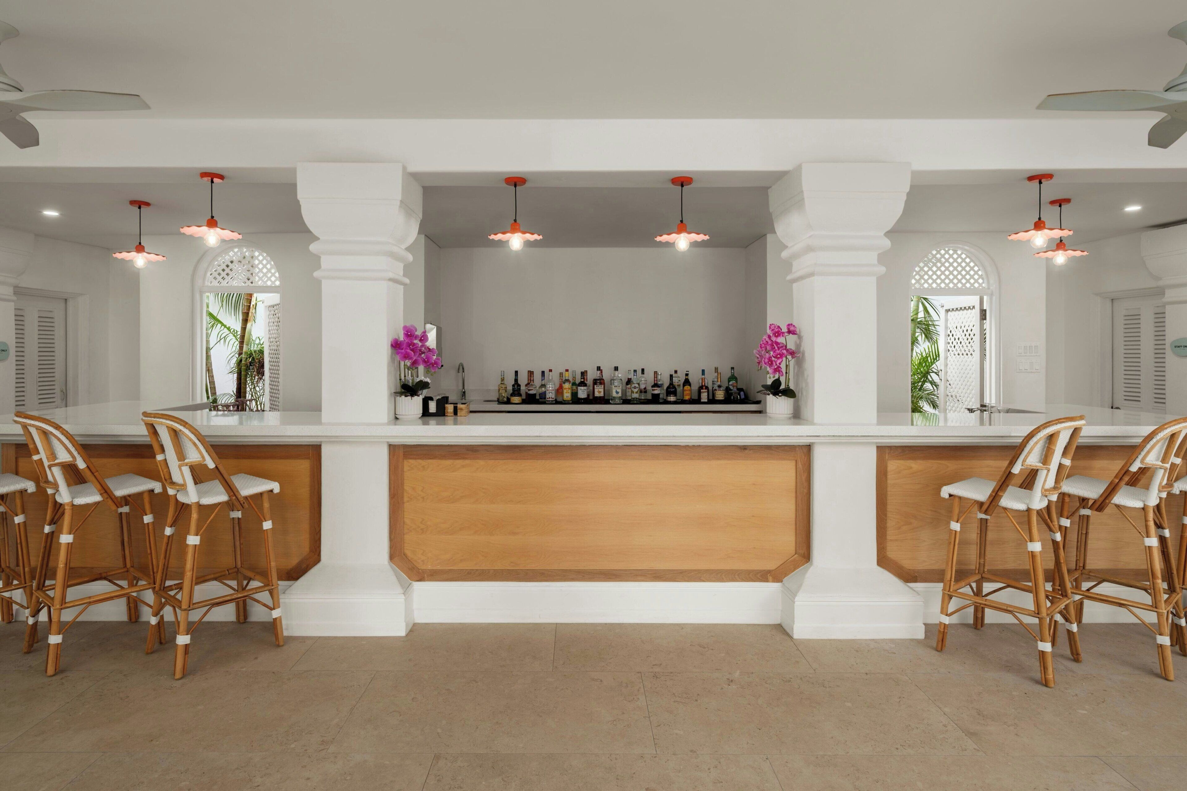A bar area with a white counter, multiple bottles, and two chairs.