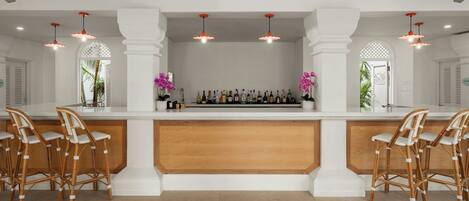 A bar area with a white counter, multiple bottles, and two chairs.