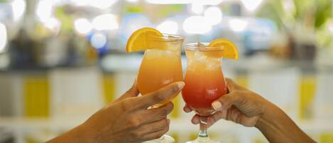 Two hands holding glasses of drinks with orange slices.
