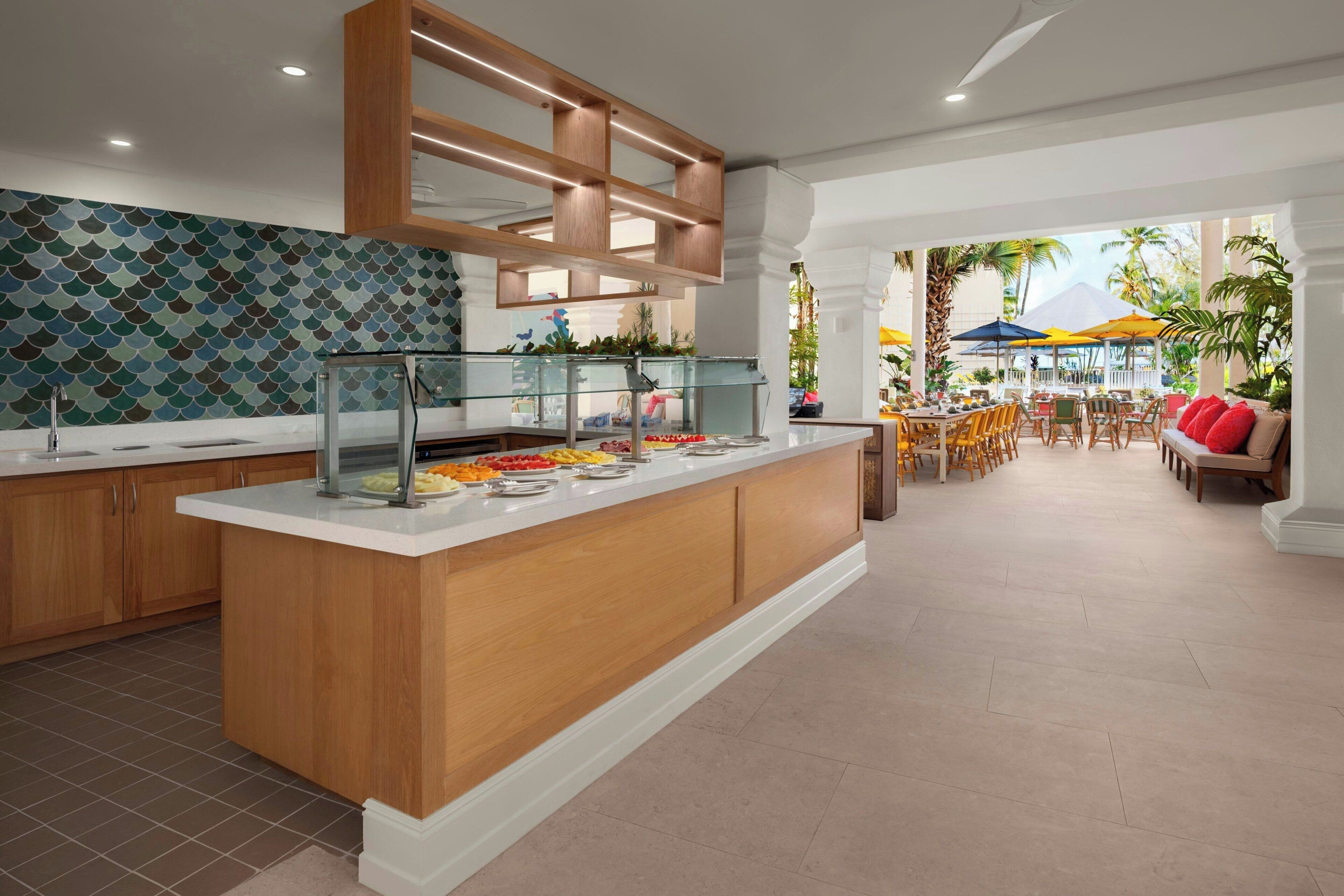A modern kitchen with a central island, a dining area with outdoor seating, and a view of the outdoors.