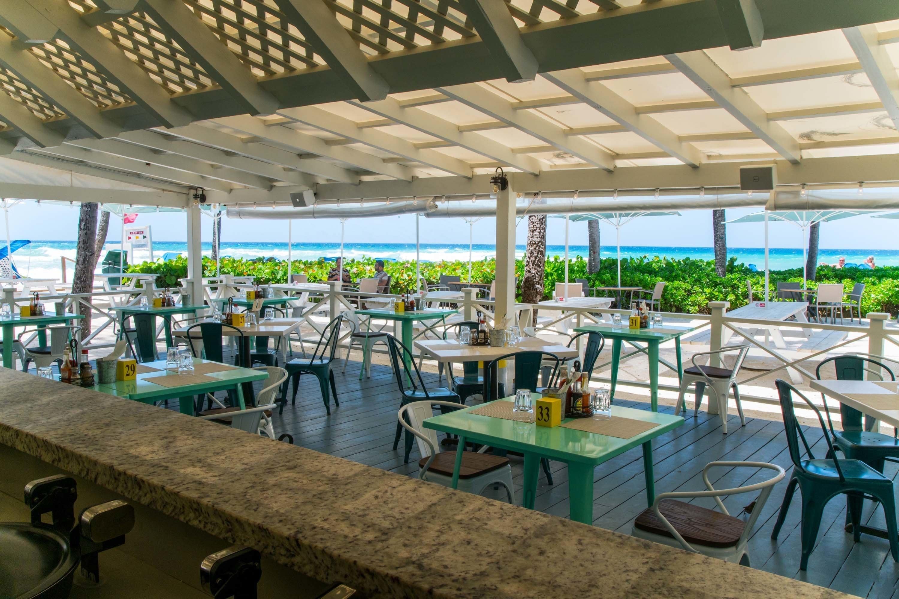 An outdoor dining area with tables and chairs, a view of the ocean, and a covered seating area.