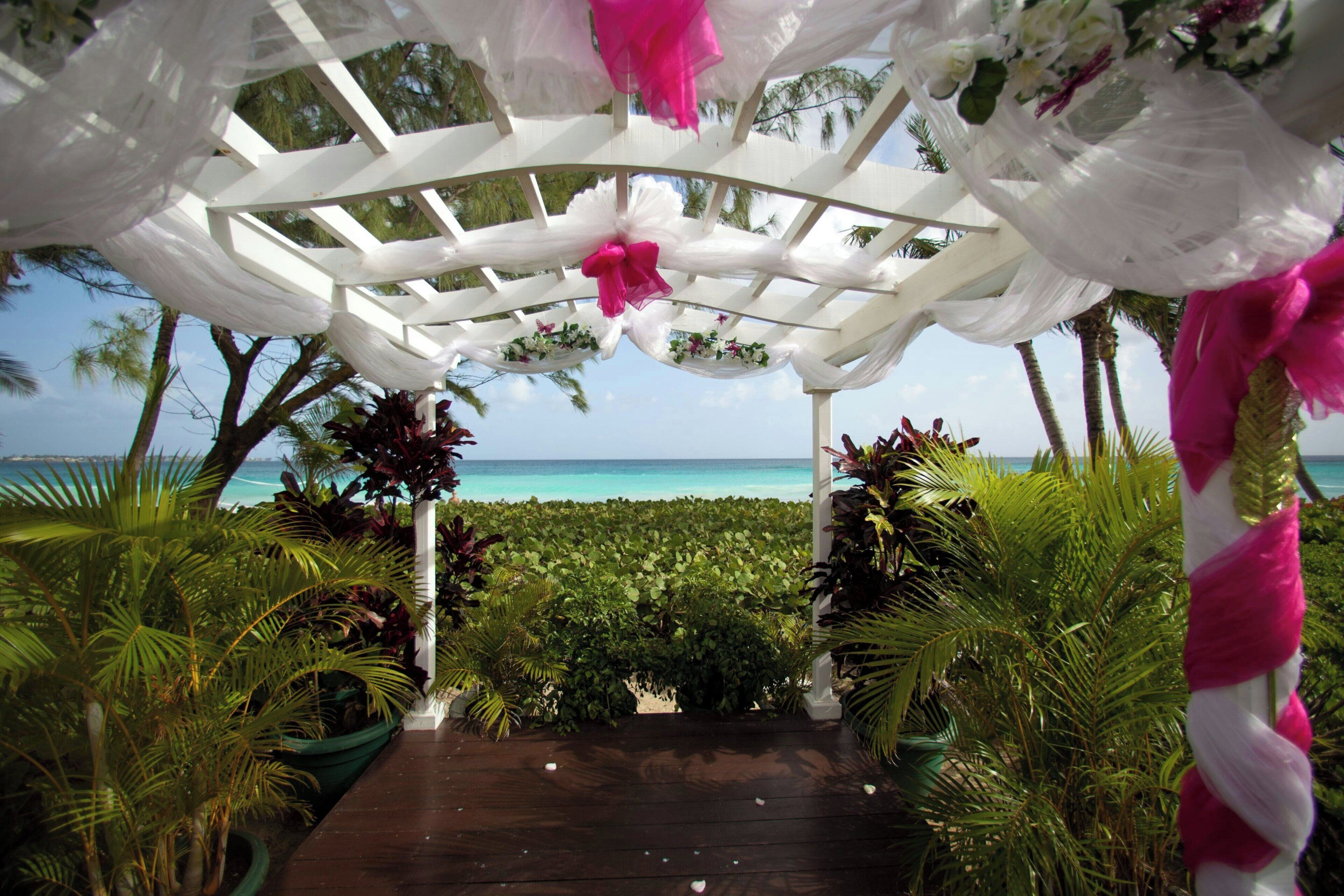 A wooden pathway leading to a white gazebo with a view of the ocean.