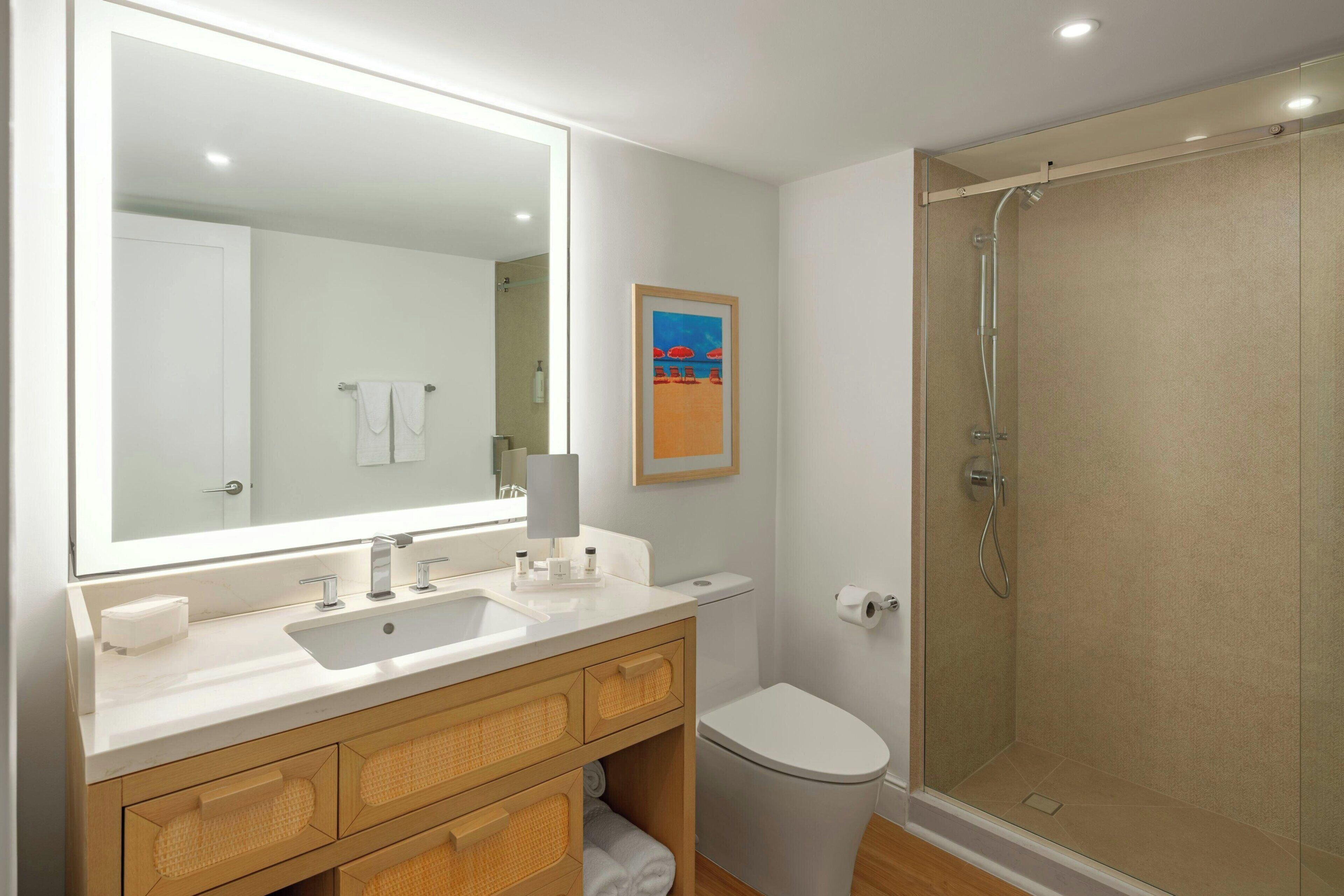 A bathroom with a large mirror, a sink, a toilet, and a glass-enclosed shower.