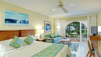 Habitación de hotel con cama, sofá, escritorio, televisor y balcón con vista al océano.