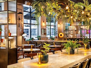 A restaurant interior with tables, chairs, hanging plants, and pendant lights. - Novotel London Bridge (London)