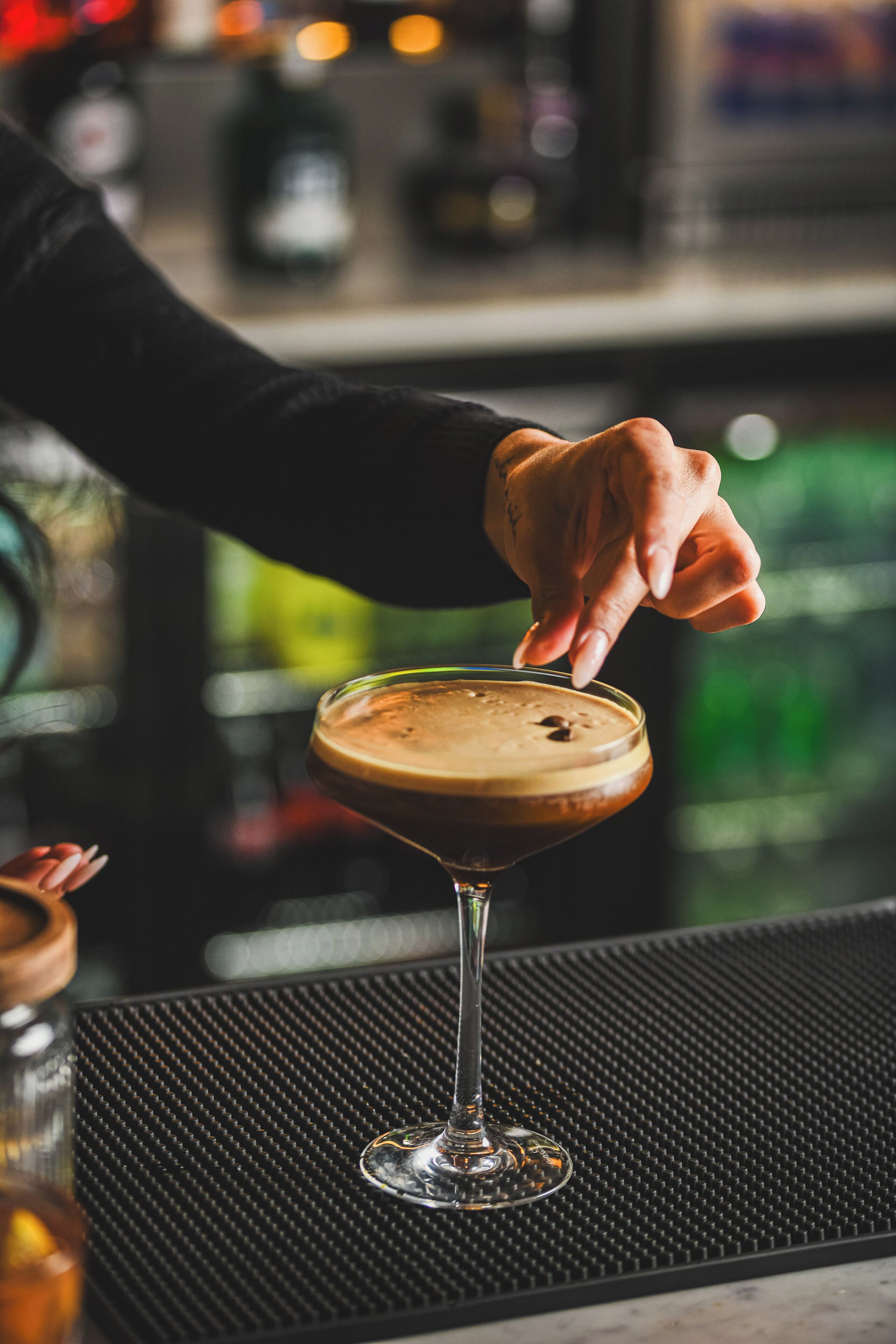 Una mano sirviendo una bebida espumosa en una copa de martini sobre la barra.