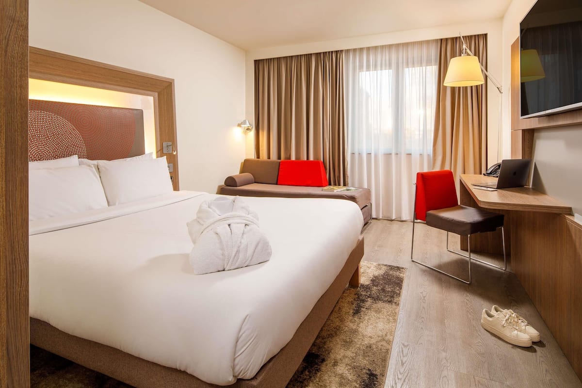 A hotel room with a large bed, a desk, a chair, and a TV.