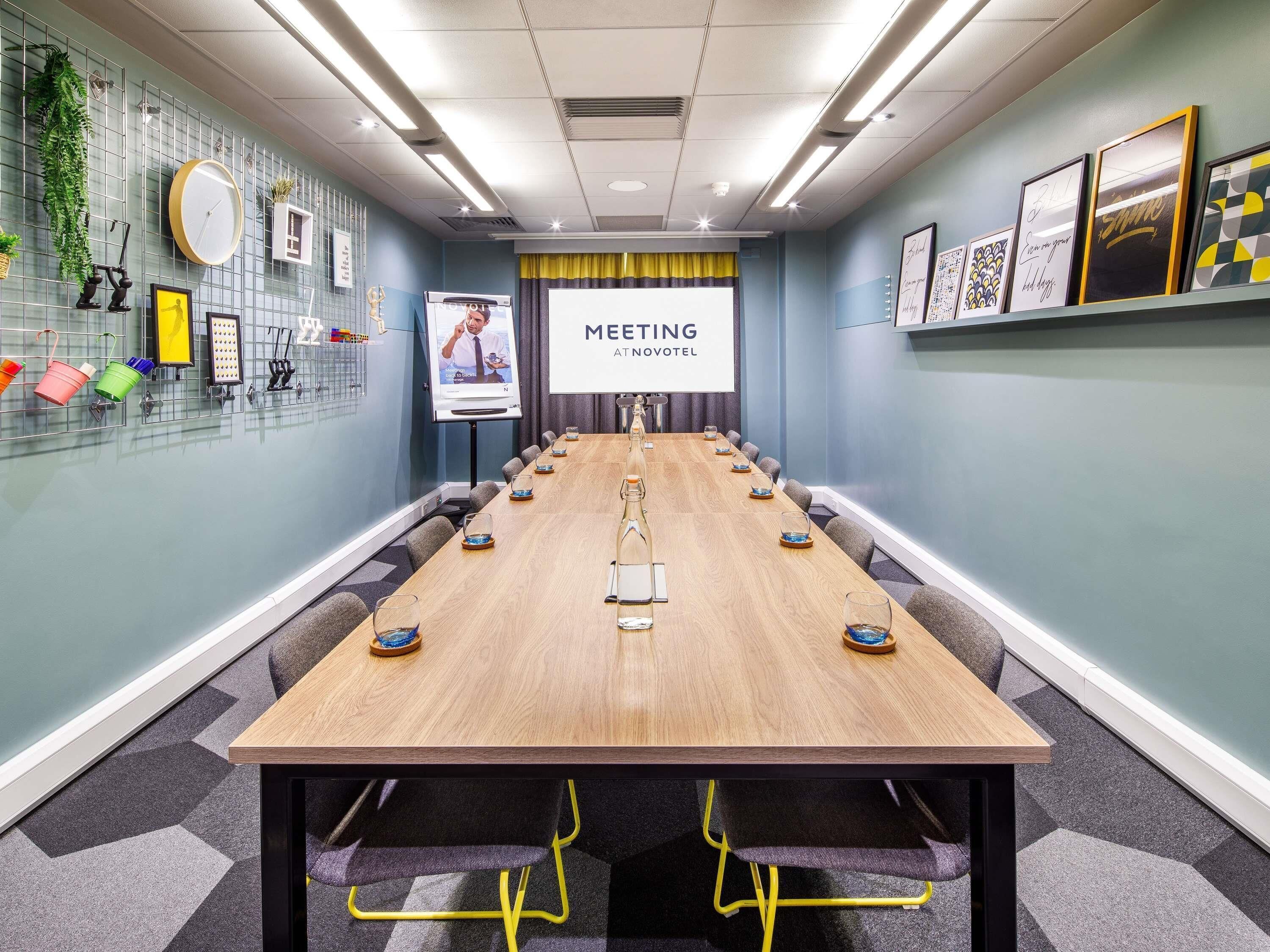 A meeting room with a long table, chairs, a projector screen, and framed artwork on the walls.