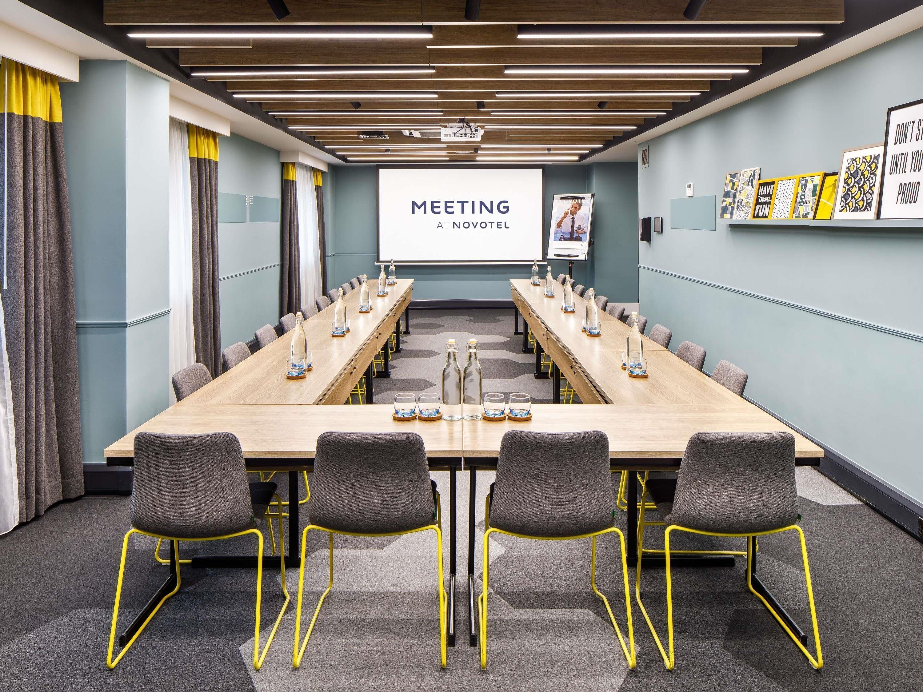 A meeting room with a long table, chairs, a projector screen, and motivational posters.
