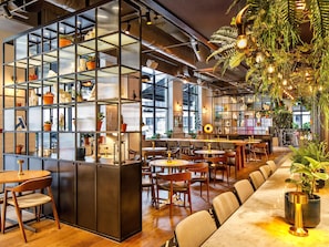 A modern interior with a long counter, multiple seating areas, and a variety of plants.