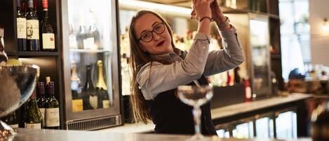 Um bartender em um bar com prateleiras cheias de garrafas de vinho e uma geladeira ao fundo.