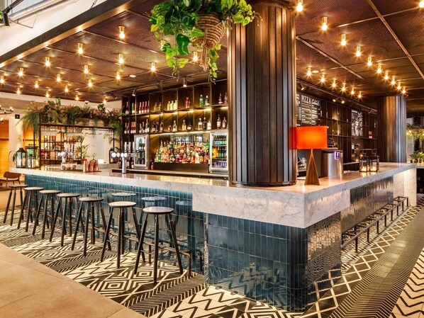 A bar area with a counter, stools, and a variety of bottles. - Novotel London Bridge (London)