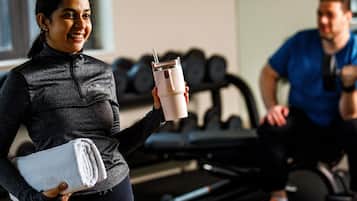 A gym with exercise equipment and a person holding a towel and a drink.