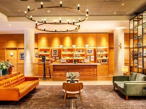 A hotel lobby with a central reception desk, wooden paneling, a large chandelier, and seating areas. - Novotel London Bridge (London)