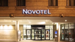 The exterior of a Novotel hotel with a glass entrance, a revolving door, and a sign above the entrance.