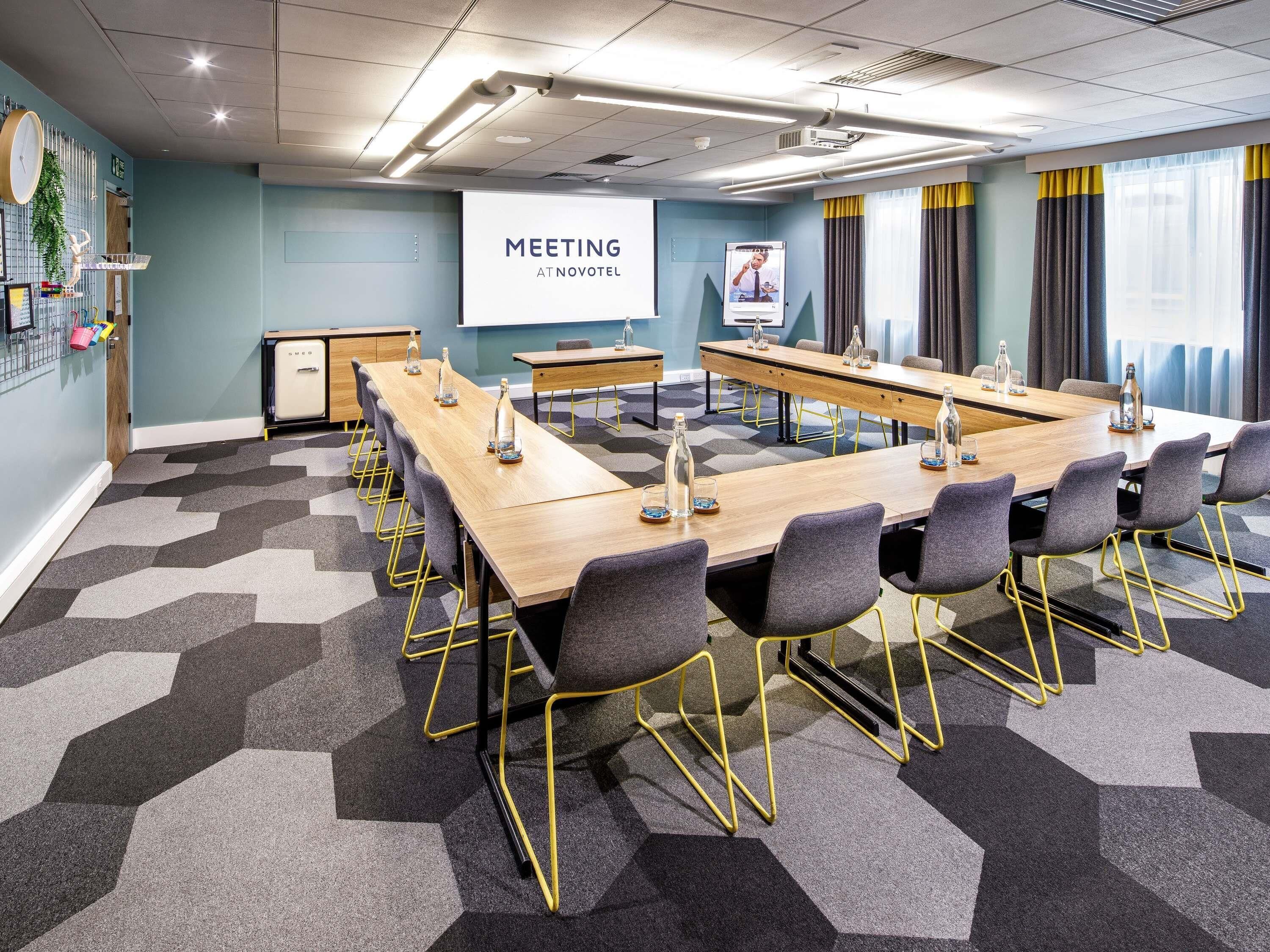 A meeting room with a long table, chairs, a projector screen, and a clock on the wall.