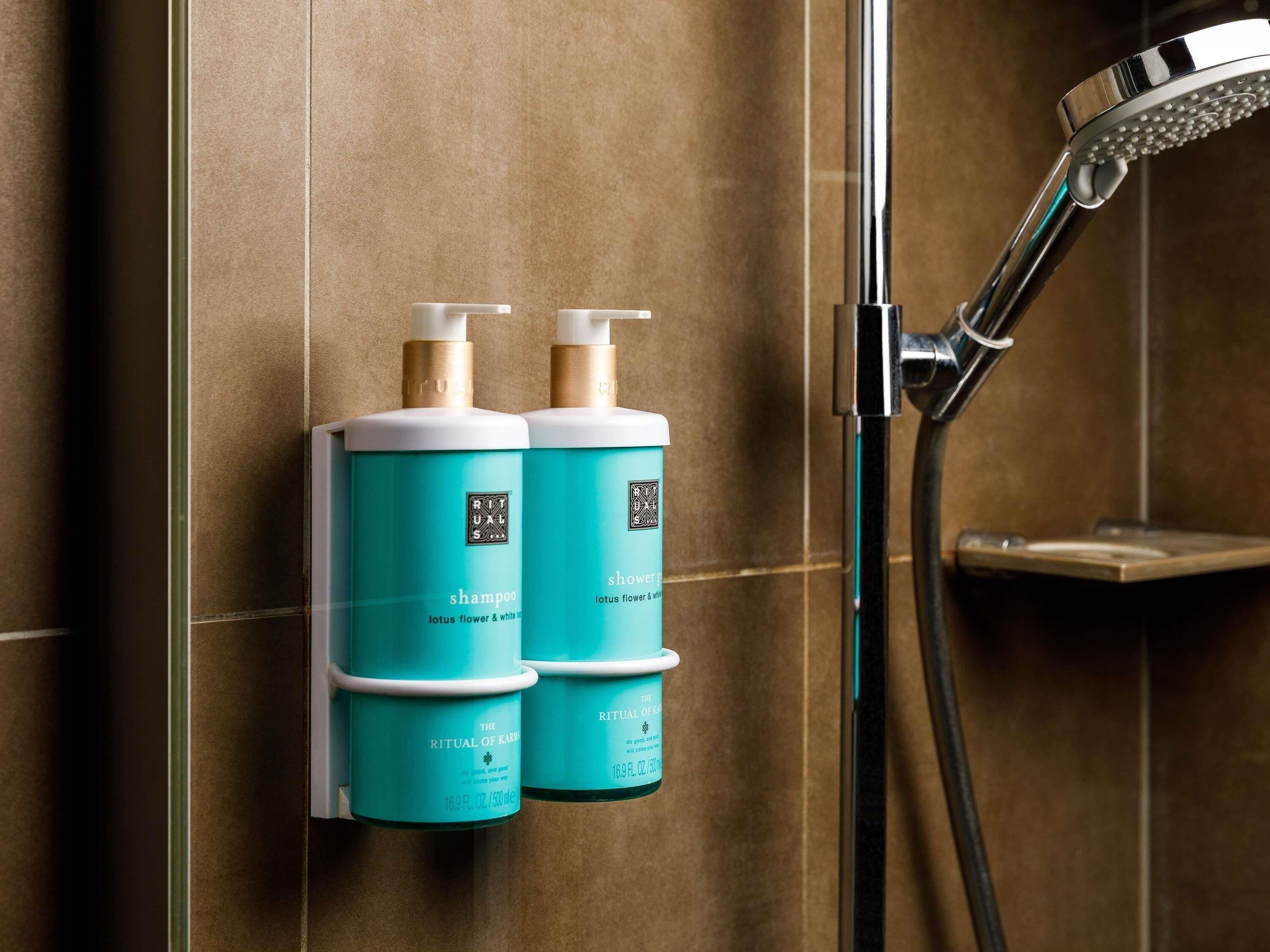 Two bottles of Ritual of Karu shampoo and shower gel in a bathroom with a showerhead.